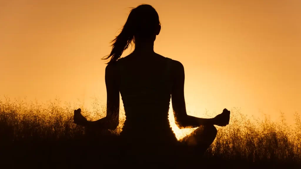 mulher no pôr do sol praticando conexão com a espiritualidade através da meditação